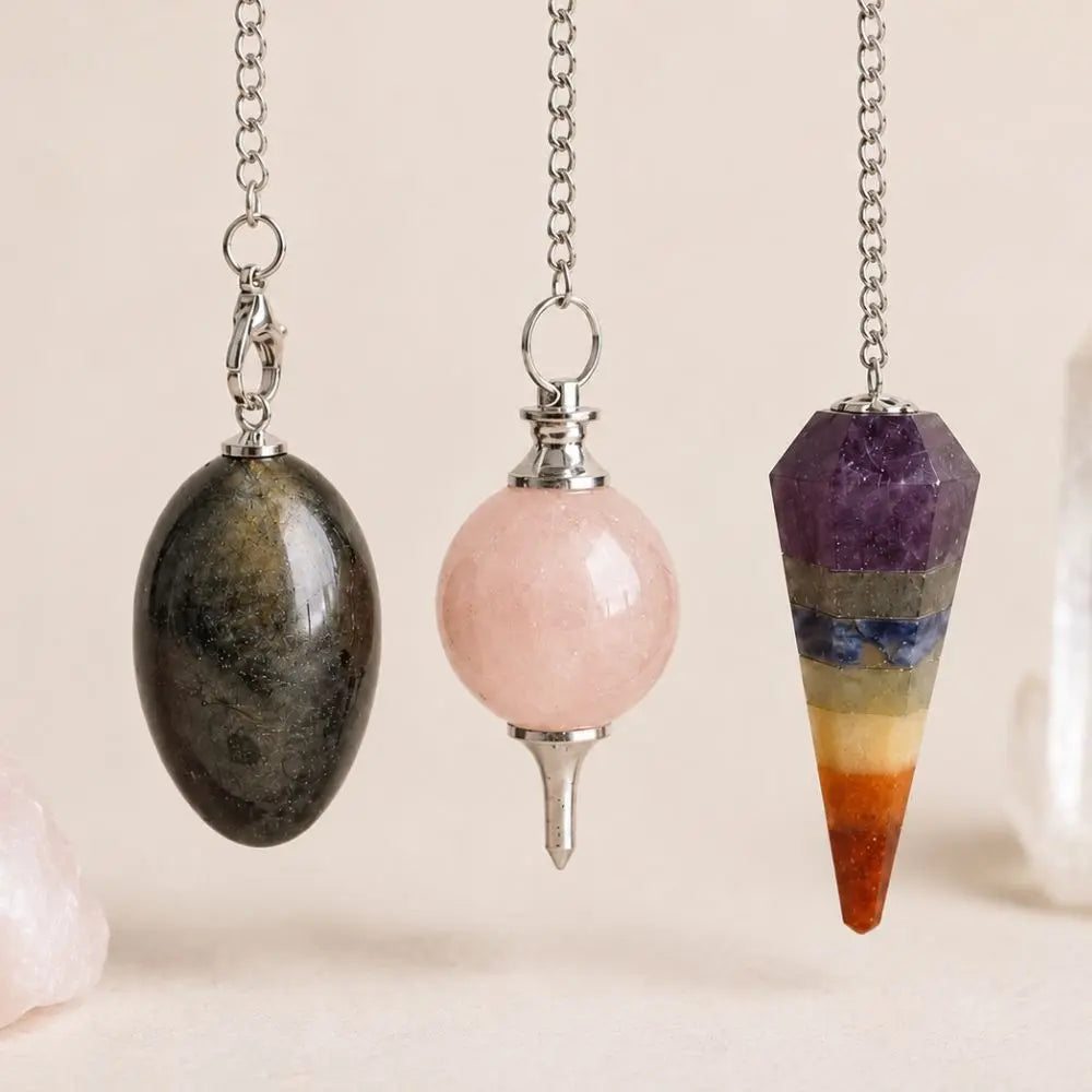 Pendules en pierres naturelles en obsidienne dorée, quartz rose et 7 chakras suspendus devant des cristaux.