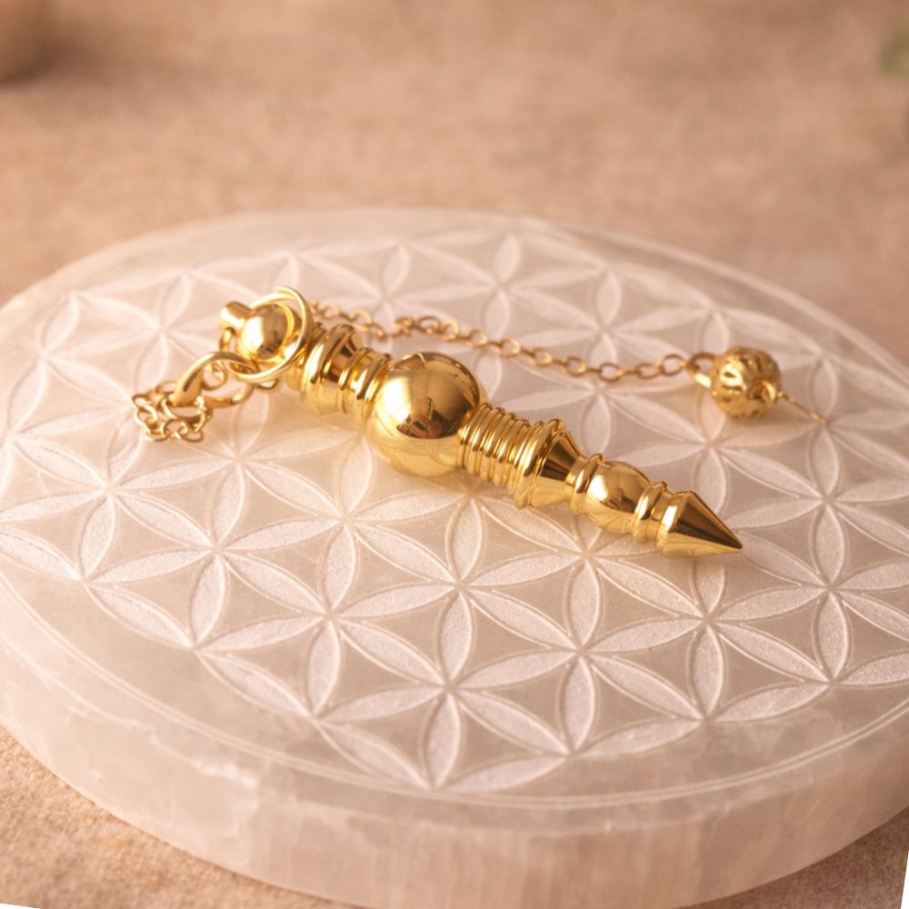 Pendule bâton en métal doré posé sur une fleur de vie en sélénite